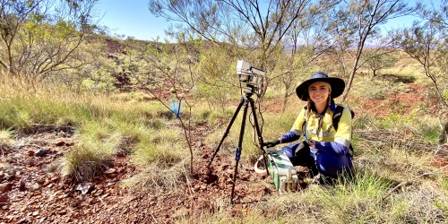 A scientist sitting in an arid landscape with surverying equipment to their right