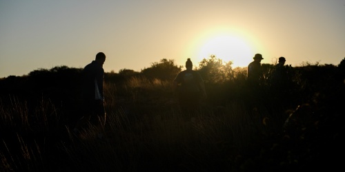 Graduate officers are silhouetted against the setting sun.