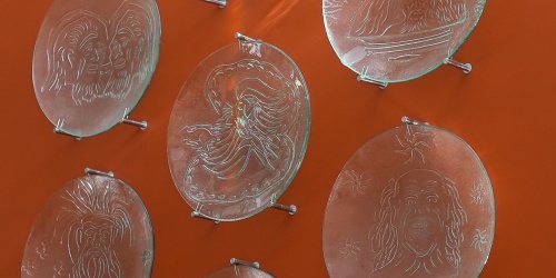 Seven glass plates carved with artworks mounted on an orange wall