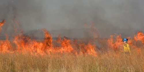 A woman stands in firefighting gear in front of a burning field doing prescribed burns