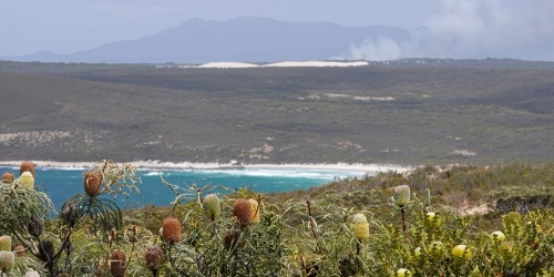 A landscape with ocean and mountains in the distance, with smoke from a bushfire far away