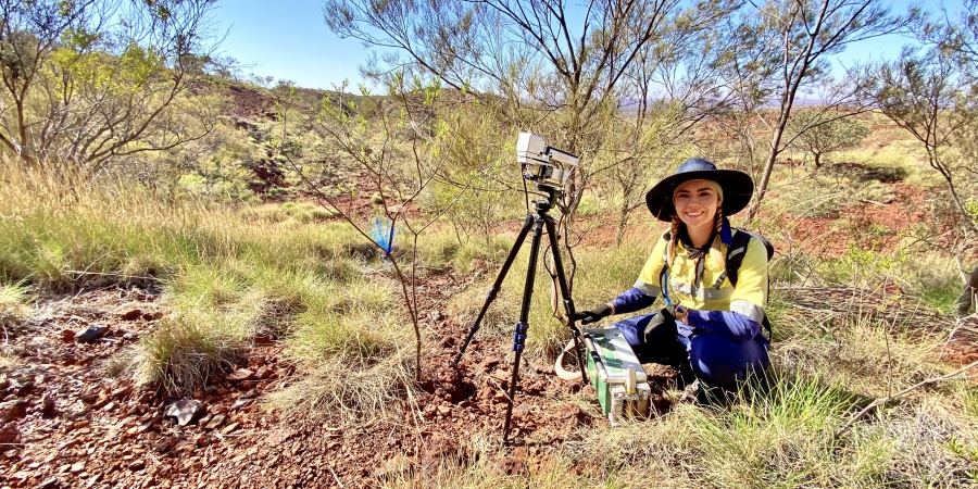 A scientist sitting in an arid landscape with surverying equipment to their right