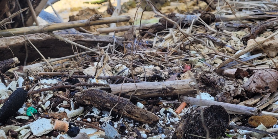 A riverbank with small pieces of plastic visible between sand and sticks