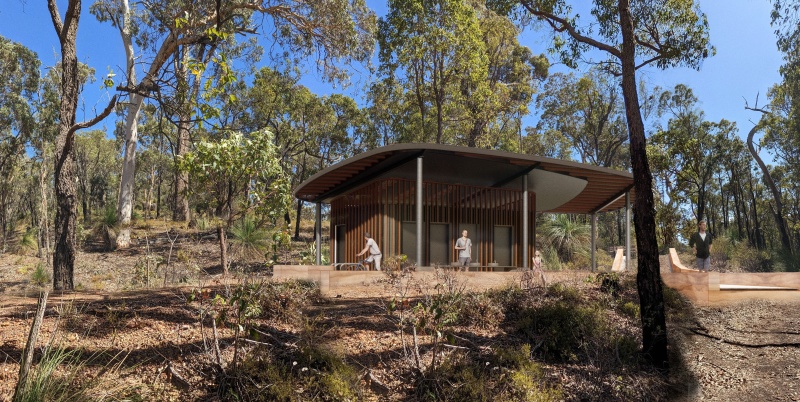 A modern pavilion with a curved roof sits in native bushland, surrounded by eucalyptus trees and low shrubs. Several people stand or walk nearby, including one with a bicycle. Bright sunlight and a clear blue sky highlight the natural setting.