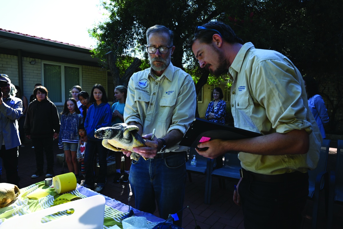 Tony Tucker holding a turtle with school children observing in the background
