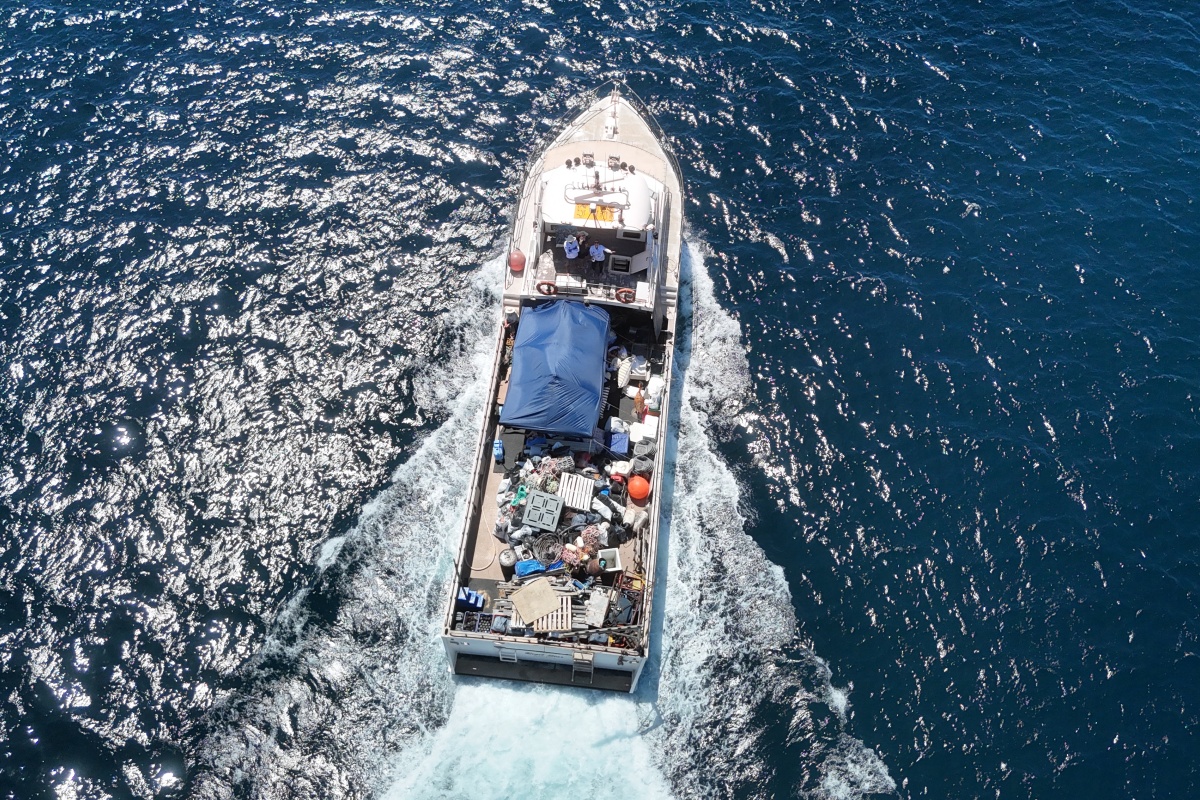 A drone shot of a boat full of marine debris, driving on the water. 