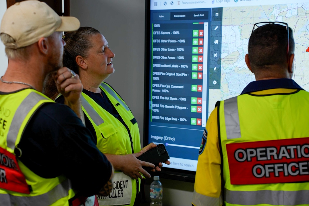 Two males and a female look at a large screen, making decisions on the fire incident