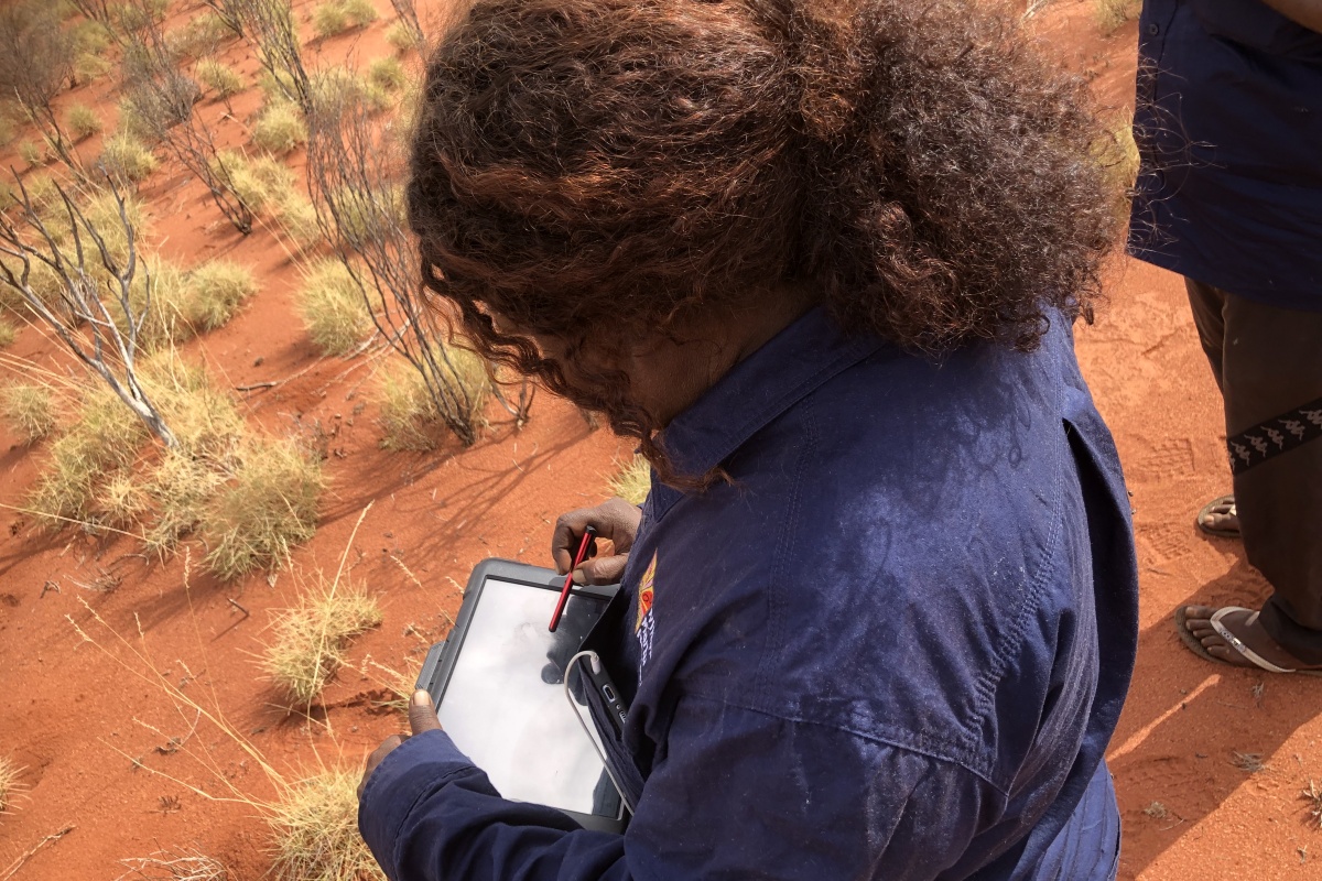 A female Indigenous ranger makes notes in the desert
