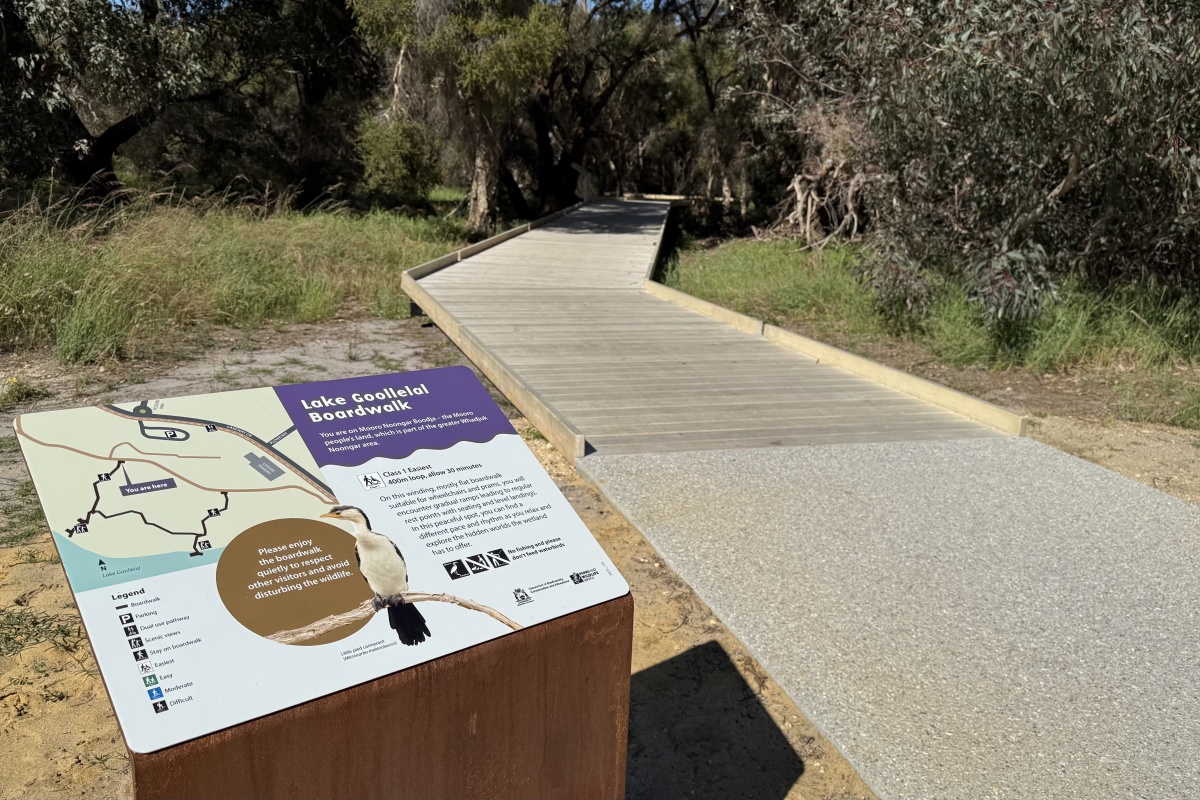 A sign with the walking trail map of the boardwalk and a path leading into the wetlands