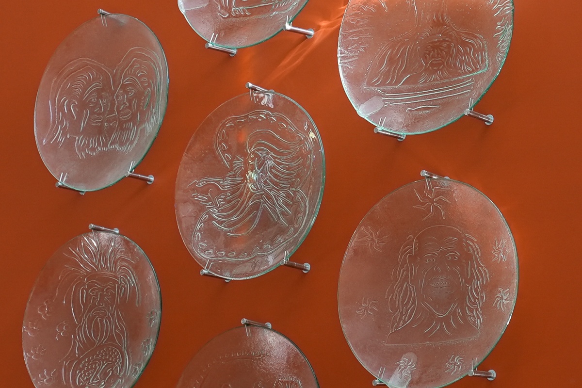 Seven glass plates carved with artworks mounted on an orange wall