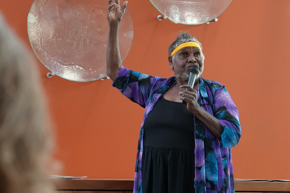 A female Aboriginal elder speaks with a microphone in front of the glass artworks