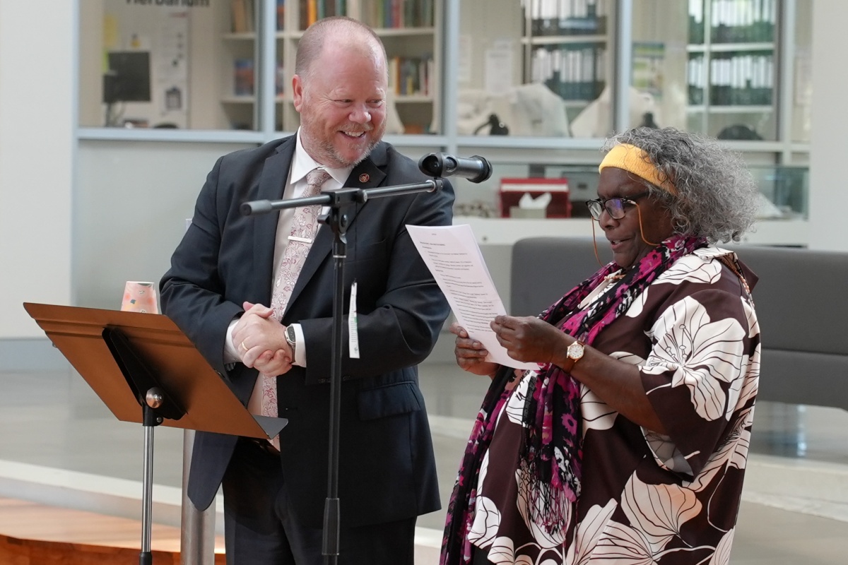 A male and female stand at the microphone, laughing, while giving a speech
