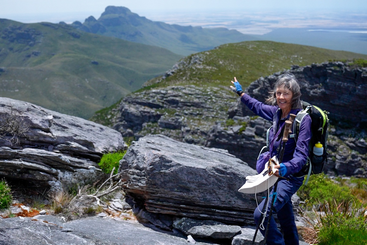A smiling woman points to the mountaintop in the background
