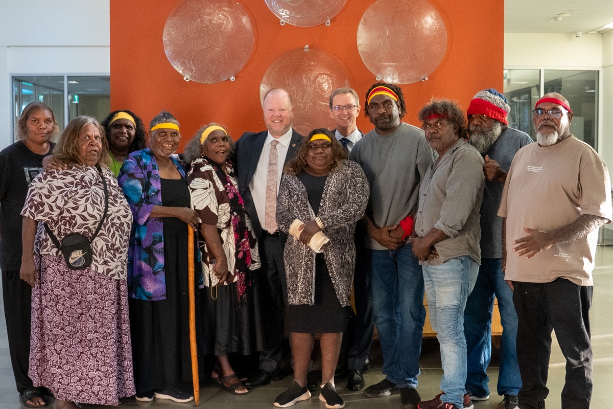 A group of Traditional Owners stand with the Minister for Environment and DBCA Director General in front of the glass artworks mounted on an orange wall