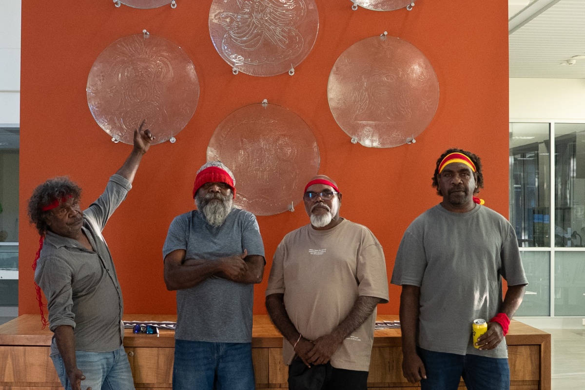 Four Aboriginal males stand in front of the glass artworks proudly