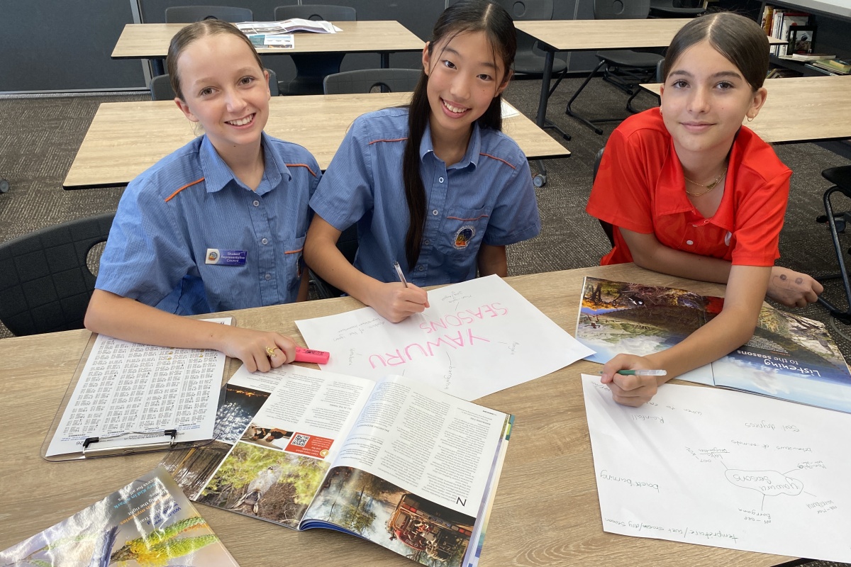 Three female high school students work at a table with issues of a magazine