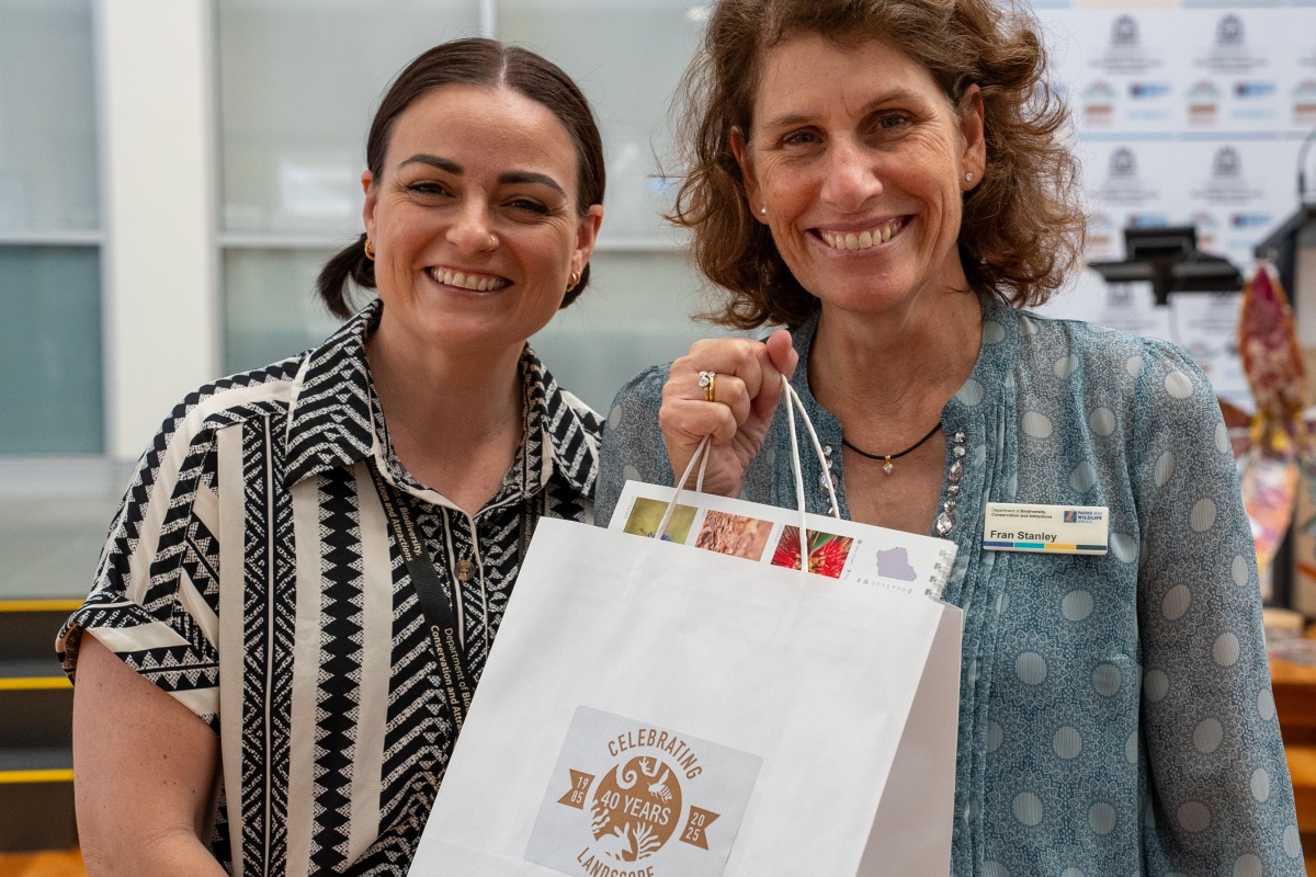 Two women smile holding a gift bag