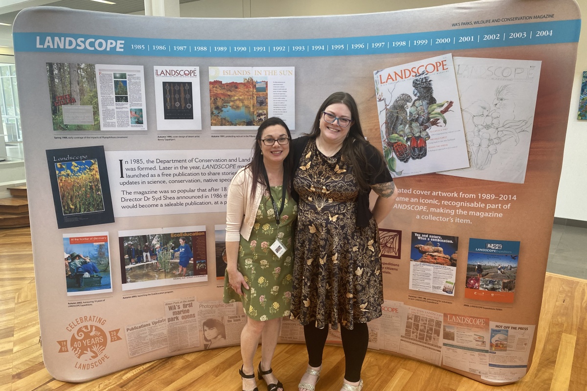 Two women stand proudly in front of a banner display