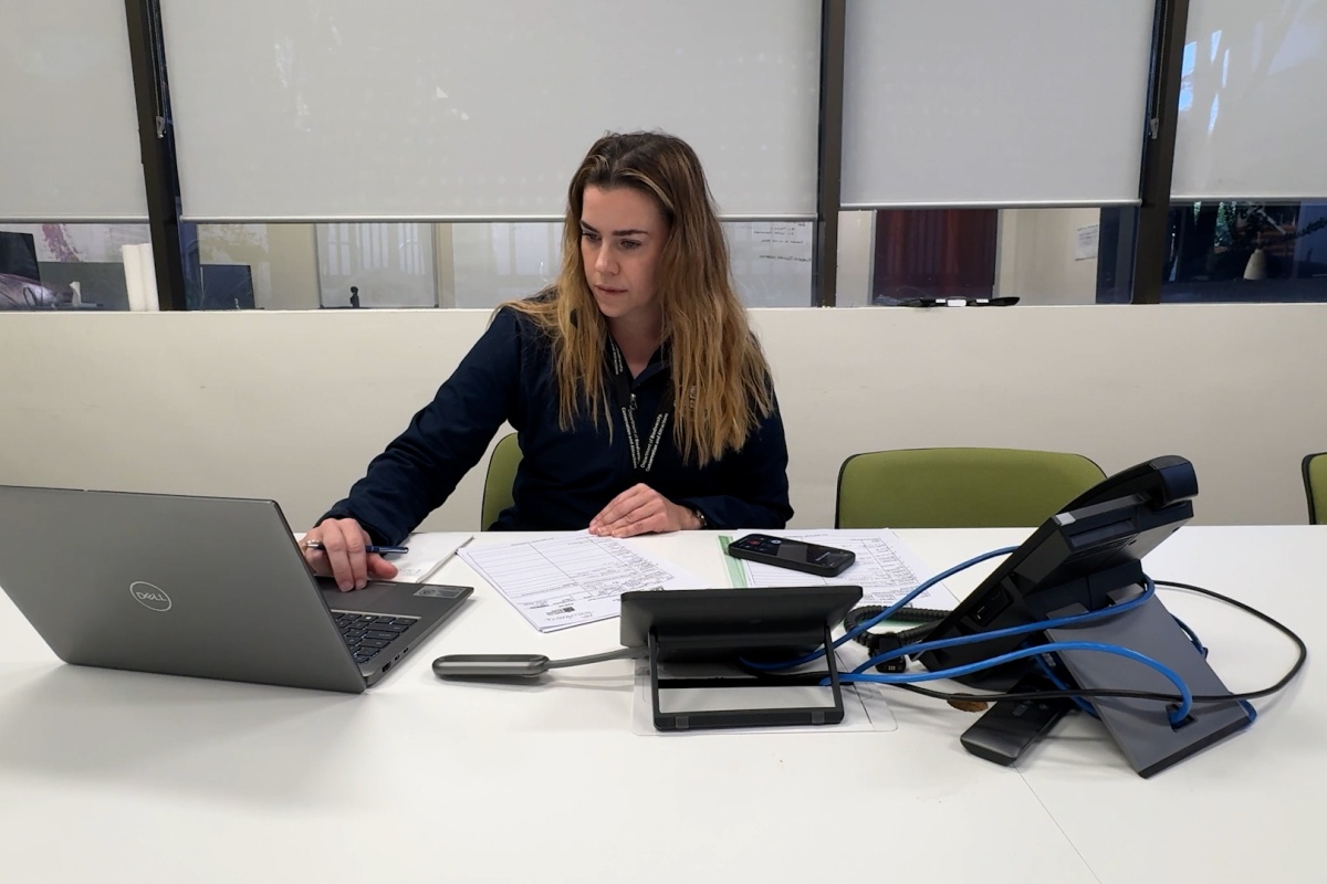 A woman works on a laptop next to paperwork and phone