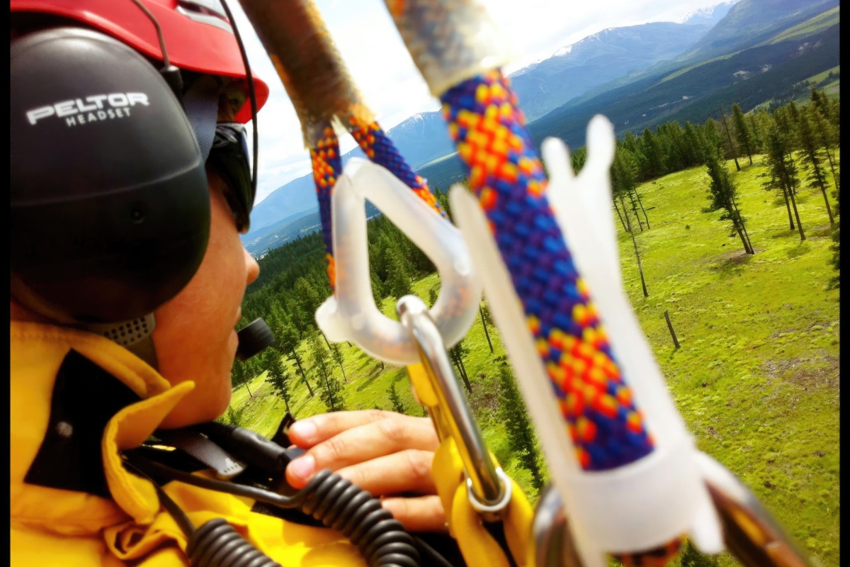 A close up of a woman in PPE attached to a helicopter flying high over the ground