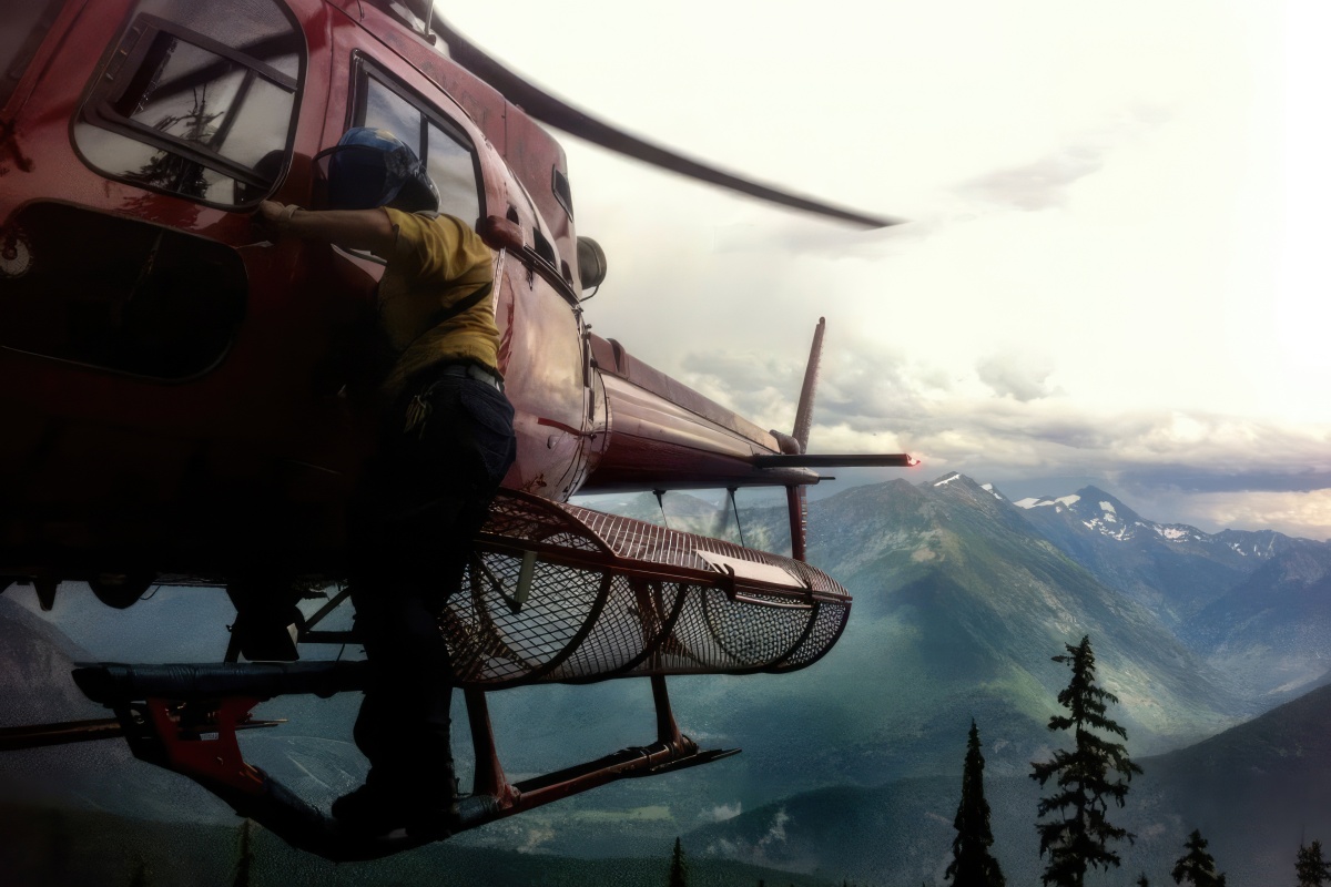 A woman stands on the outside of a helicopter about to descend into the mountains